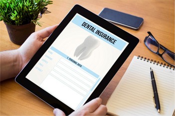 Patient holding tablet with dental insurance forms over desk