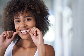 Woman with curly hair smiling while flossing her teeth