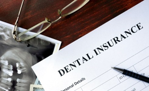 Dental insurance form lying on desk with X-ray, money, and glasses