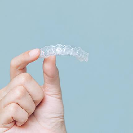 Patient holding clear aligners up against blue background