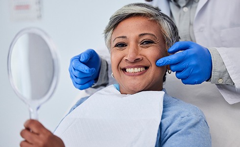 Woman smiling while holding handheld mirror in dental chair