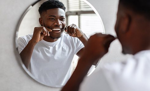 Man smiling at reflection while flossing his teeth