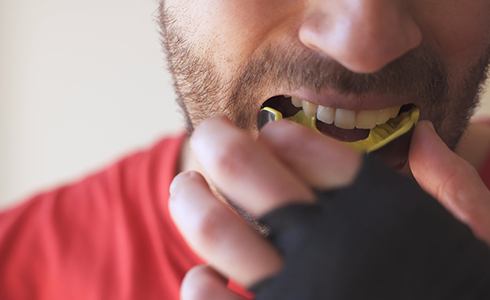 Man placing yellow and black mouthguard in his mouth