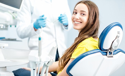 Woman in yellow shirt smiling while sitting in dental chair
