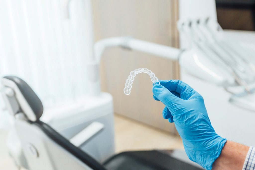 Dentist with blue glove holding Invisalign aligner