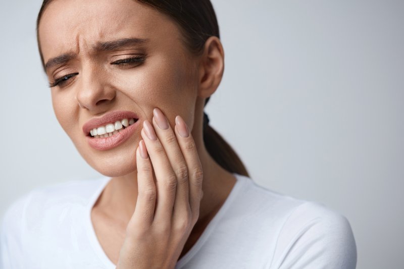 person with toothache who needs emergency dental visit holding cheek