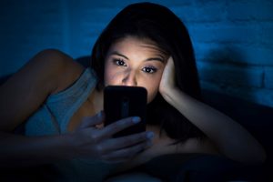 Woman in bed leaning head on hand with cell phone light shining on her face